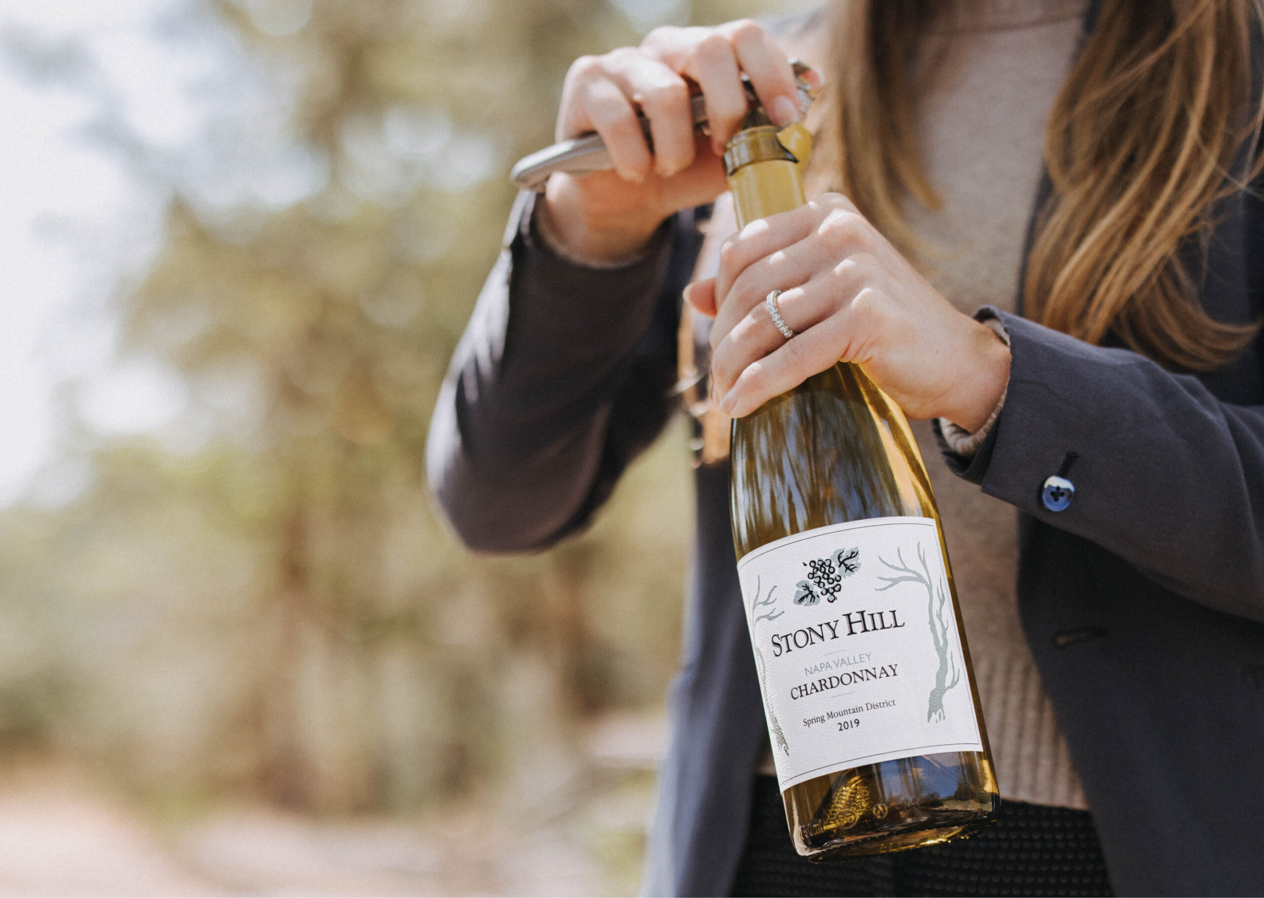 A woman opening a bottle of Stony Hill Chardonnay outdoors in the vineyard.