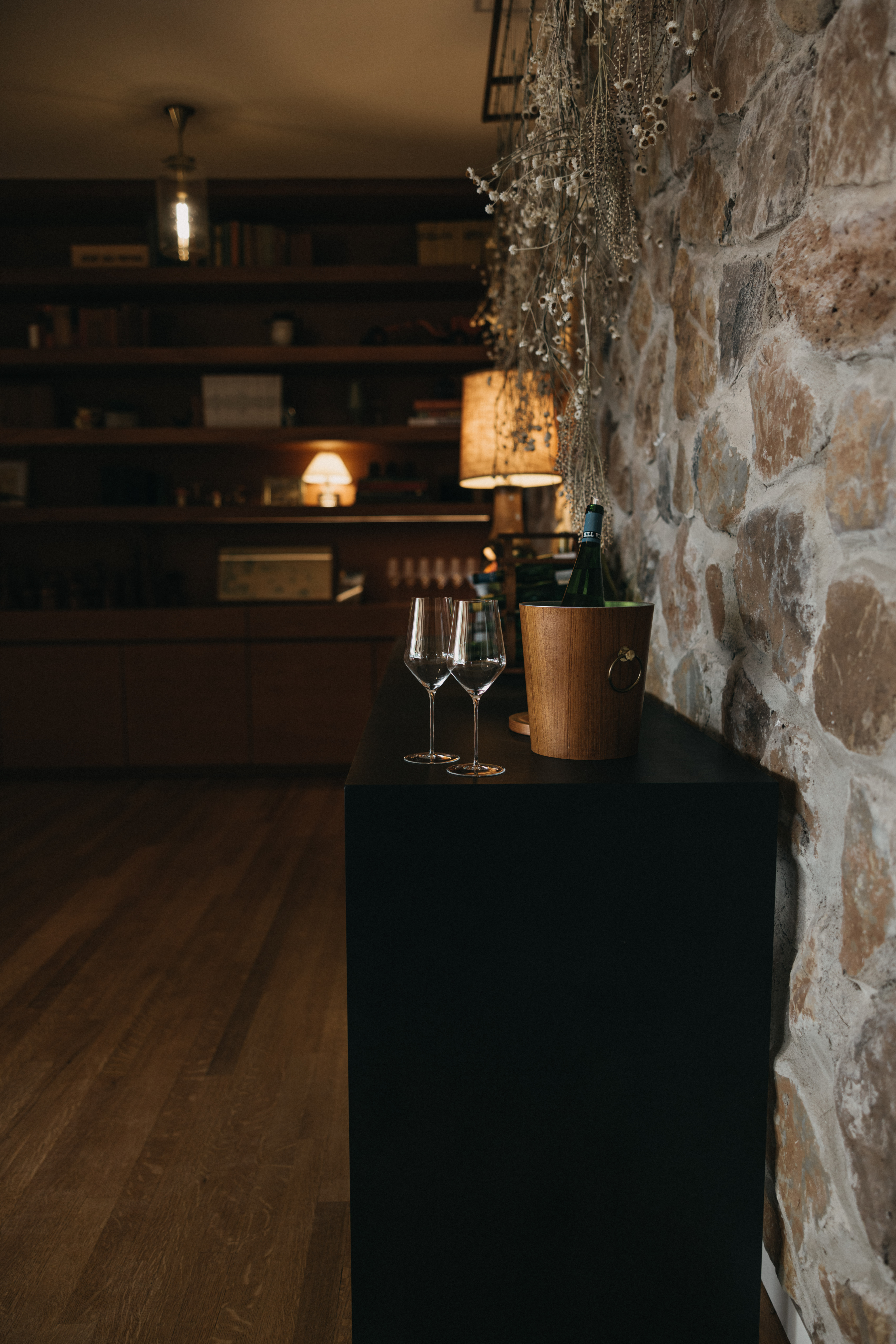 Inside the Stony Hill residence, a stone wall and table next to the wall with wine glasses and a bottle of Stony Hill.