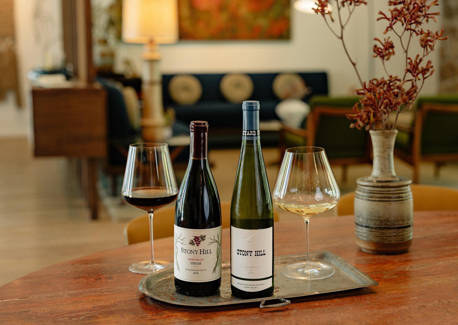 Stony Hill Seasons Traditions: a bottle of 2018 Syrah and 2020 Gewurztraminer on a table with two glasses of wine.