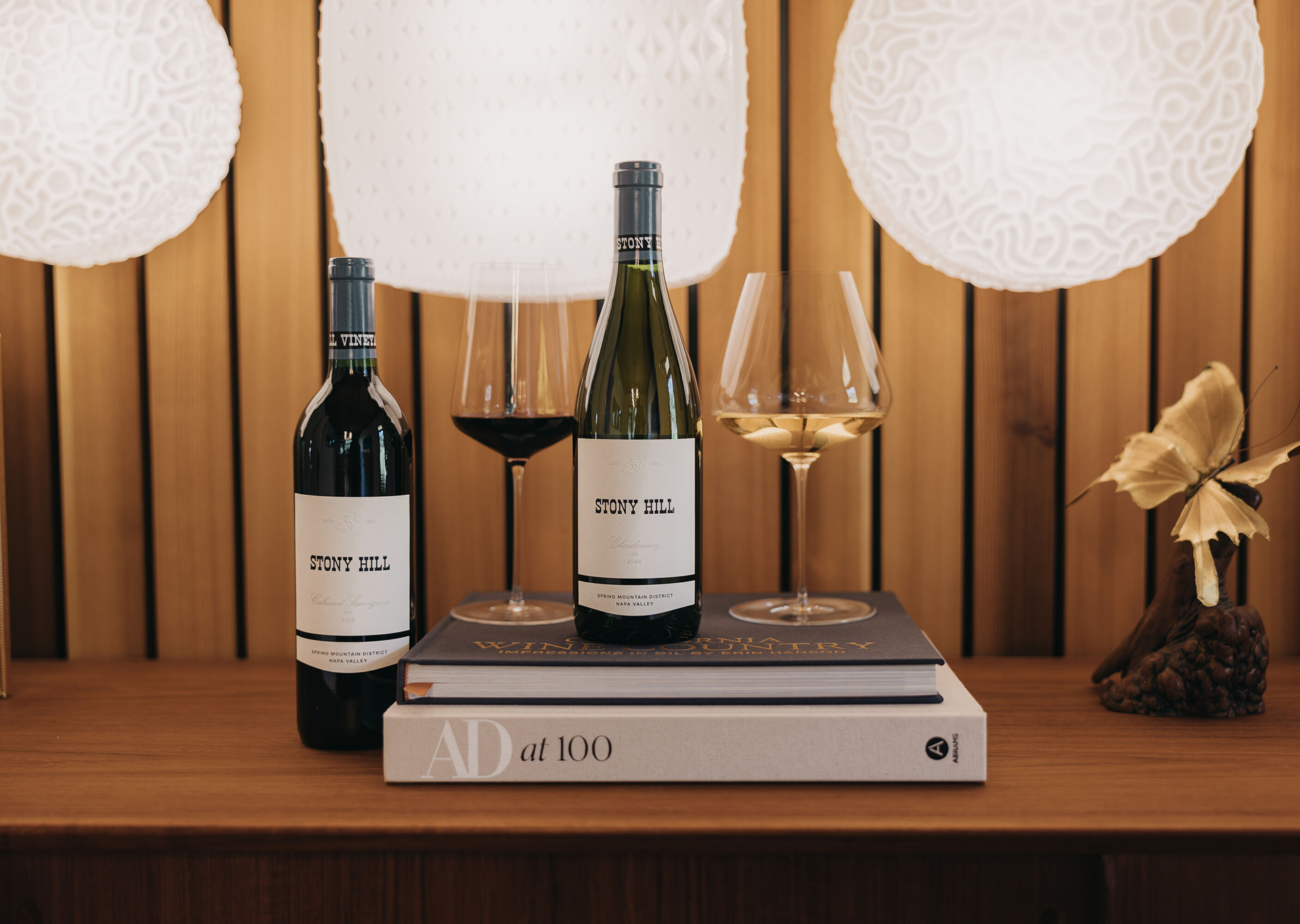 Treasures From the Cellar: A bottle of 2019 Stony Hill Cabernet Sauvignon, and 2020 Stony Hill Chardonnay on a table with a stack of books and two glasses of wine.