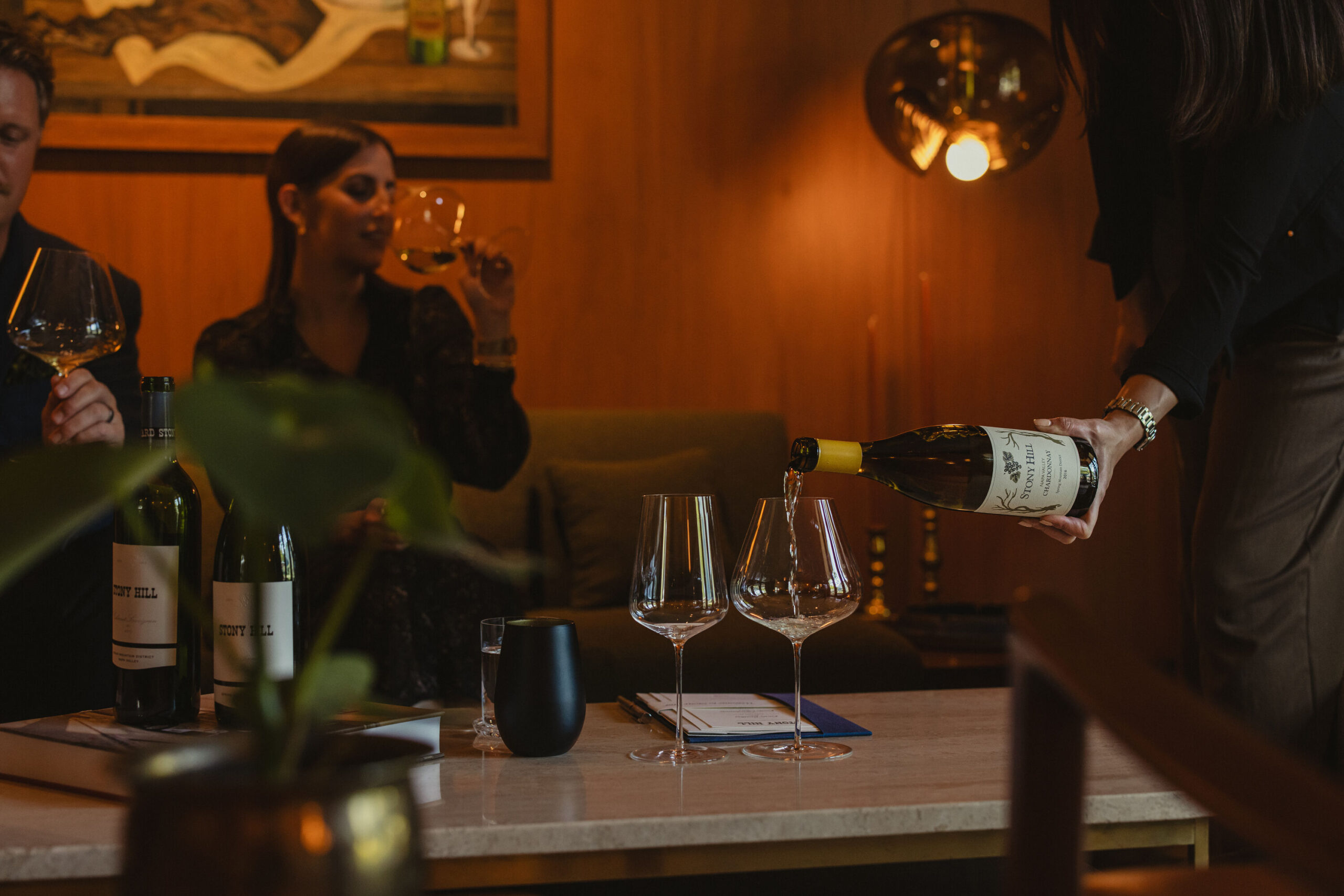 A couple enjoying a tasting at the Stony Hill Residence. Wine glasses filled with wine and bottles of Stony Hill on a coffee table.