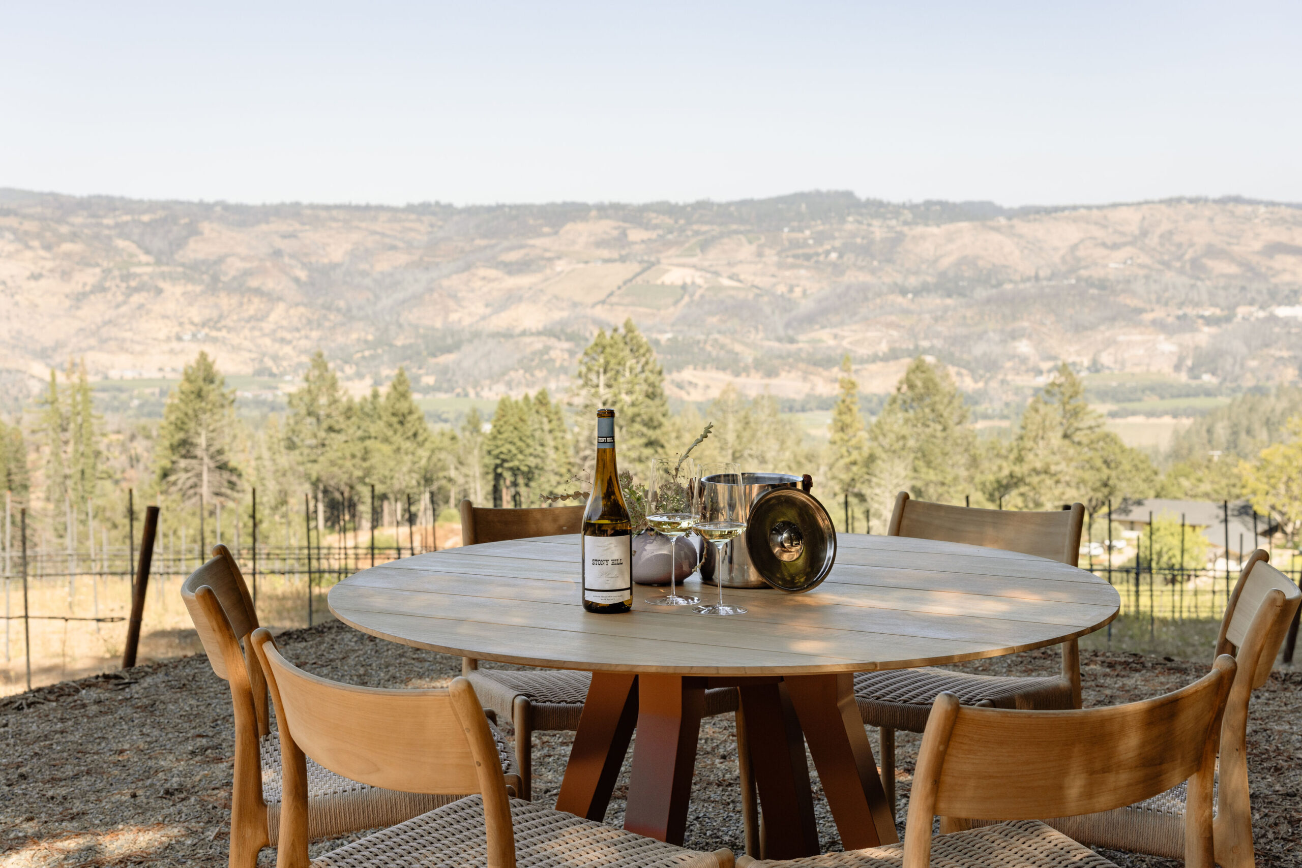 A table outside the Stony Hill Residence overlooking Napa Valley with a bottle of Stony Hill Chardonnay on the table and two glasses of wine.