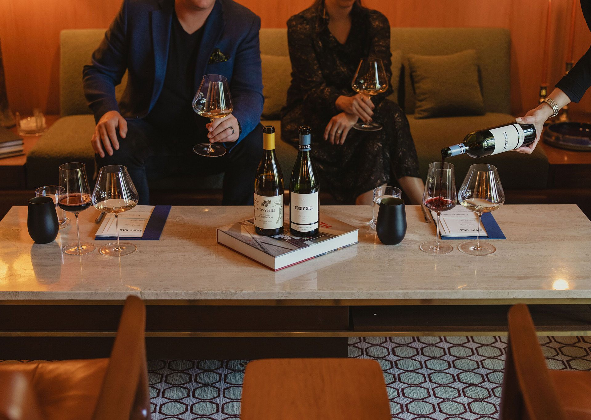 A couple enjoying a tasting at the Stony Hill Residence. Wine glasses filled with wine and bottles of Stony Hill on a coffee table.