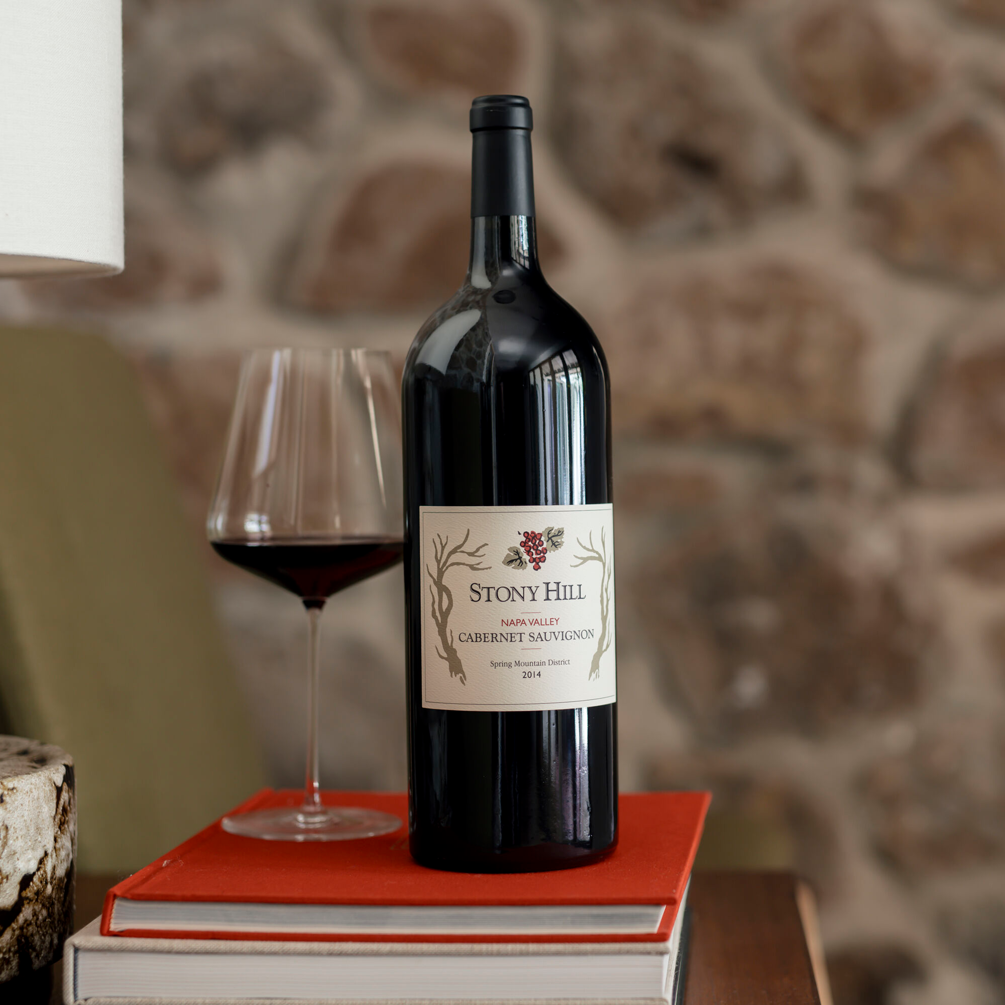 Stony Hill Cabernet Sauvignon Magnum 10 Years: A bottle of 2014 Cabernet Sauvignon on a table on top of books next to a glass of wine.