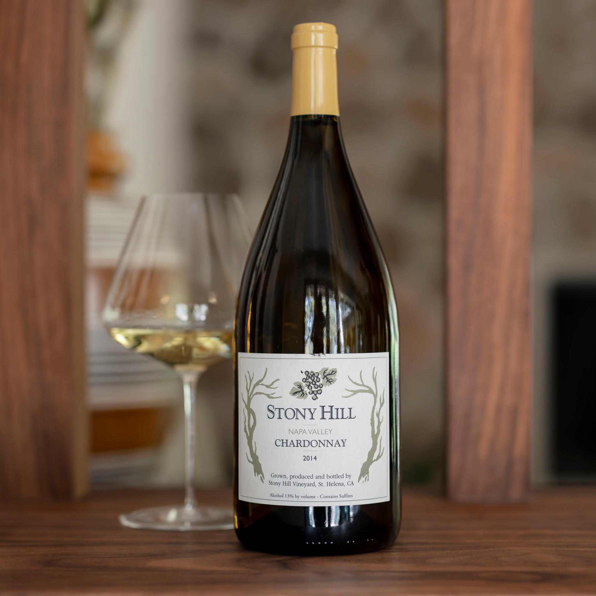 Stony Hill Chardonnay Magnum 10 Years: A bottle of 2014 Chardonnay on a table next to a glass of wine.