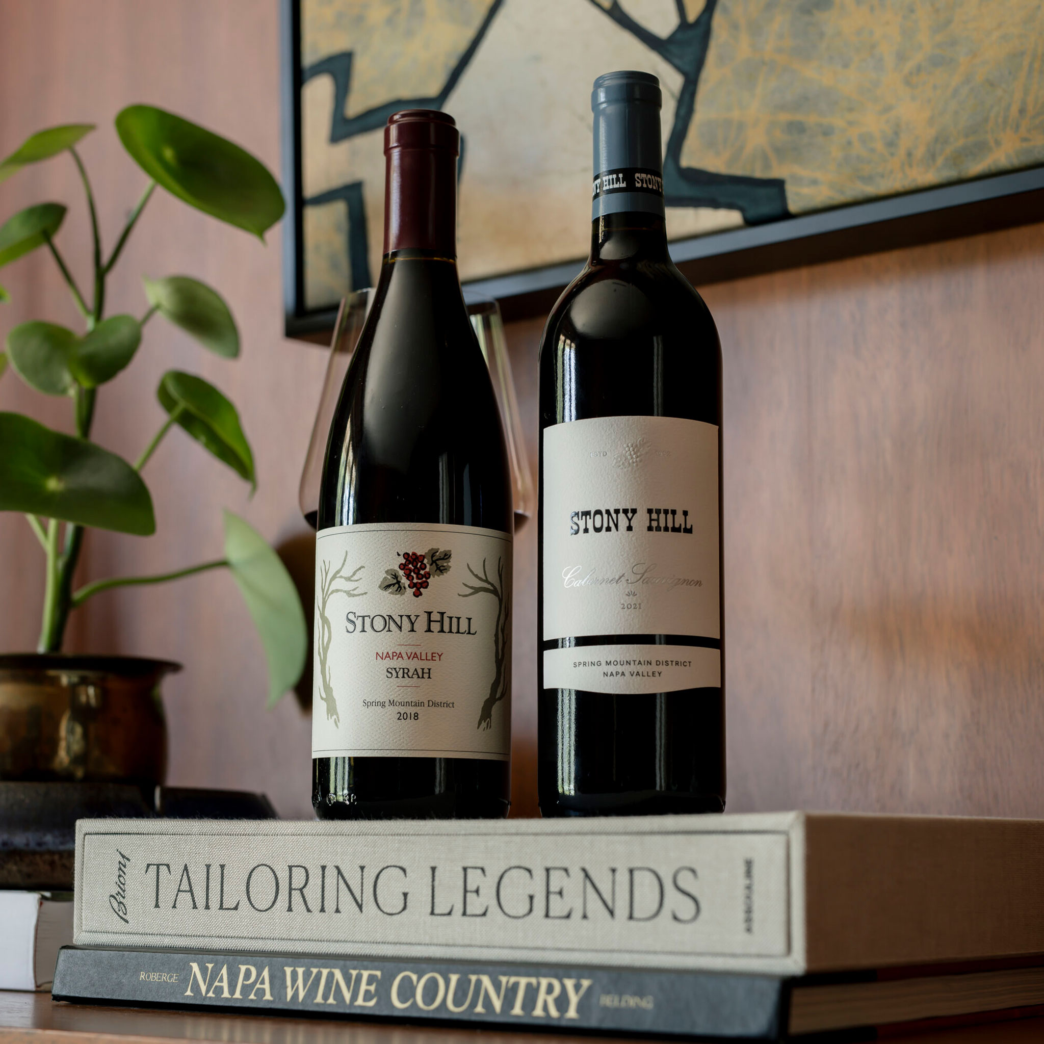 Stony Hill Two Vintages, Two Varietals: a bottle of 2018 Syrah and 2021 Estate Cabernet Sauvignon on a table, on top of books.